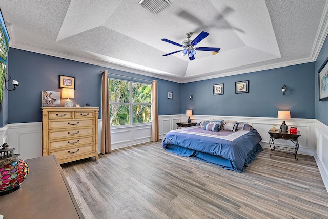 4474 Thornwood Cir, Palm Beach Gardens, FL 33418 - bedroom with a textured ceiling, a tray ceiling, wood finished floors, a wainscoted wall, and a decorative wall