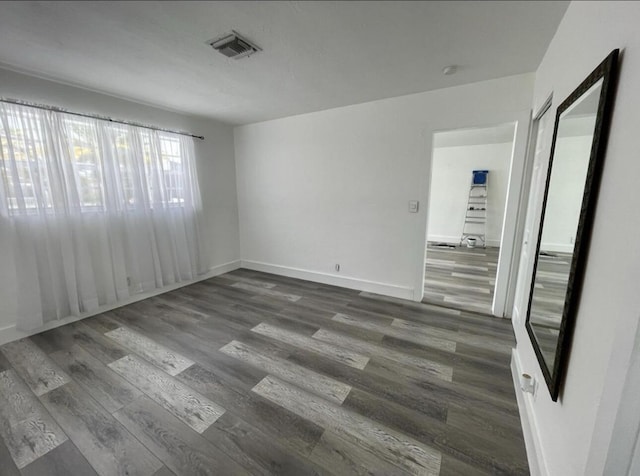 empty room featuring baseboards, dark wood-type flooring, and visible vents