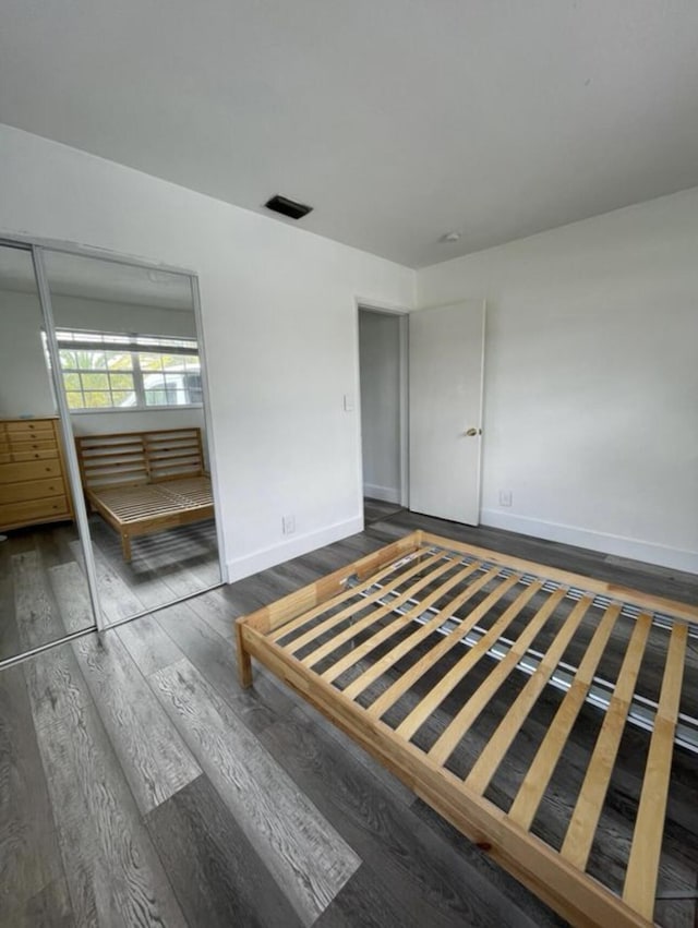 unfurnished bedroom featuring baseboards, wood finished floors, visible vents, and a closet