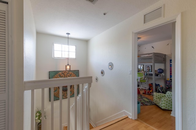 corridor with visible vents, baseboards, light wood finished floors, a notable chandelier, and an upstairs landing