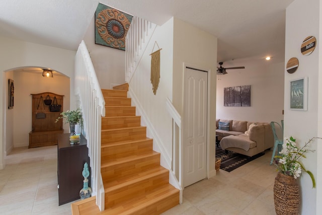 stairway featuring baseboards, arched walkways, a ceiling fan, and tile patterned floors