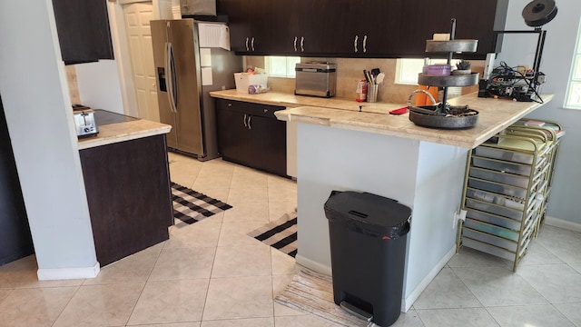 kitchen featuring light countertops, stainless steel refrigerator with ice dispenser, decorative backsplash, and light tile patterned floors