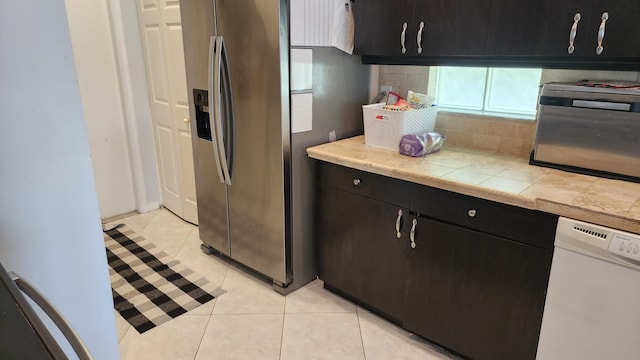 kitchen with backsplash, stainless steel refrigerator with ice dispenser, white dishwasher, light tile patterned floors, and dark cabinets