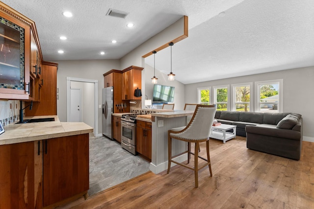 kitchen featuring visible vents, brown cabinetry, a peninsula, a sink, and stainless steel appliances