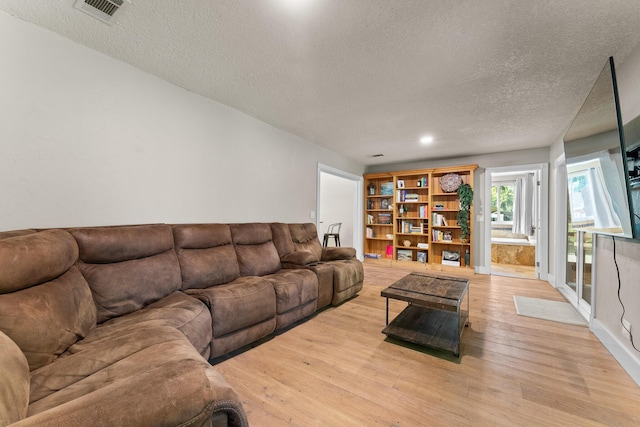 living room with light wood-style floors, a textured ceiling, and visible vents