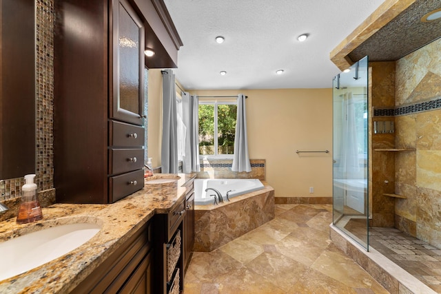 bathroom featuring double vanity, a textured ceiling, a bath, a stall shower, and a sink