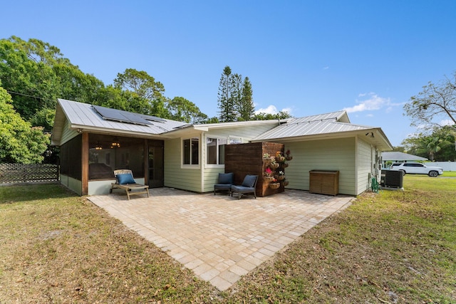 back of property with solar panels, metal roof, a lawn, a sunroom, and a patio area