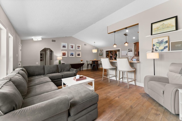 living room featuring baseboards, vaulted ceiling, visible vents, and light wood-type flooring