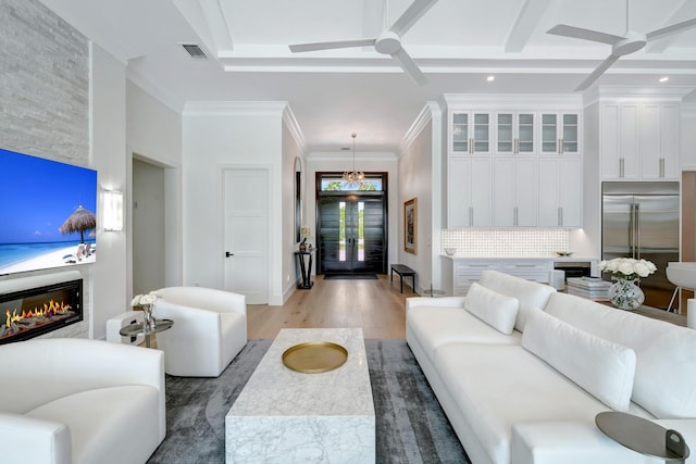 living room with visible vents, a glass covered fireplace, ceiling fan with notable chandelier, and light wood-type flooring