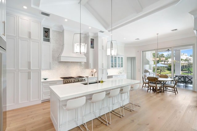 kitchen featuring decorative backsplash, a kitchen island with sink, light countertops, white cabinetry, and a sink