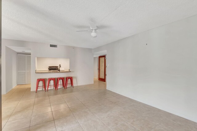 living area featuring visible vents, a ceiling fan, a textured ceiling, and light tile patterned flooring