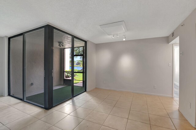empty room with baseboards, a textured ceiling, tile patterned floors, and a wall of windows
