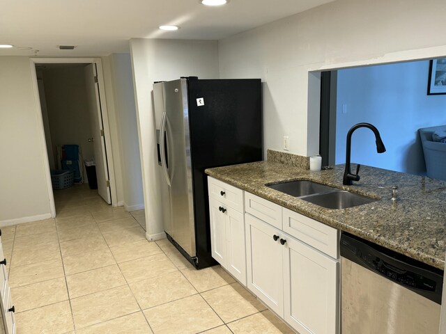 kitchen with appliances with stainless steel finishes, a sink, white cabinets, dark stone counters, and light tile patterned flooring