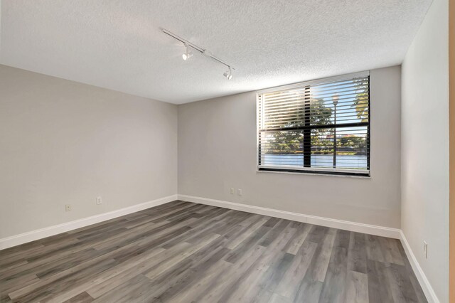 spare room featuring track lighting, a textured ceiling, dark wood-type flooring, and baseboards