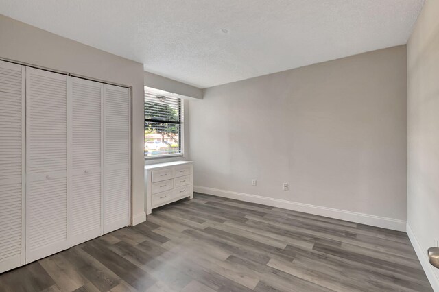 unfurnished bedroom with baseboards, a textured ceiling, dark wood-style floors, and a closet