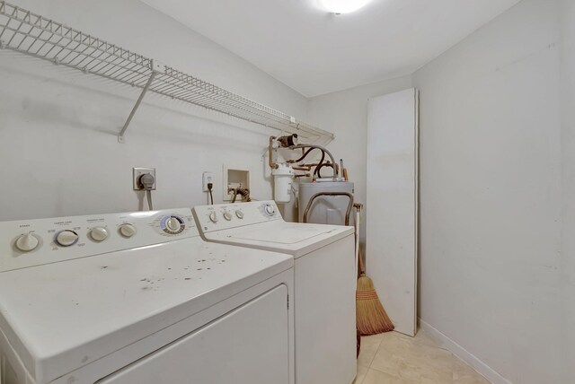 clothes washing area featuring laundry area, washing machine and dryer, baseboards, water heater, and light tile patterned floors