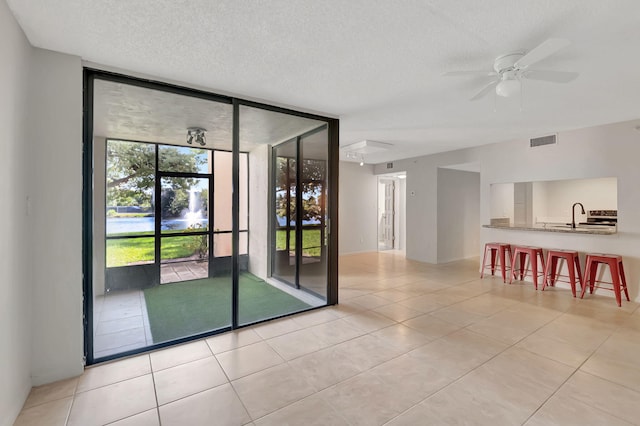 empty room featuring a sink, a ceiling fan, floor to ceiling windows, light tile patterned floors, and visible vents