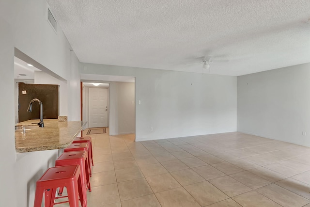 unfurnished room with visible vents, a sink, a textured ceiling, a ceiling fan, and light tile patterned floors
