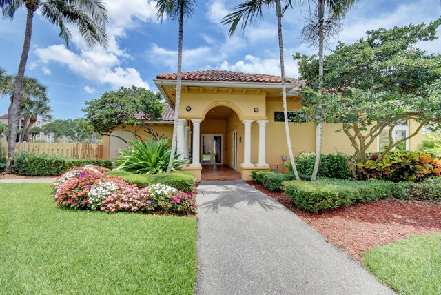 mediterranean / spanish house featuring a tiled roof, fence, a front yard, and stucco siding