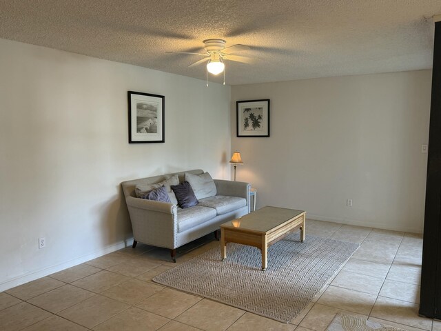 living area featuring baseboards, a ceiling fan, a textured ceiling, and light tile patterned floors
