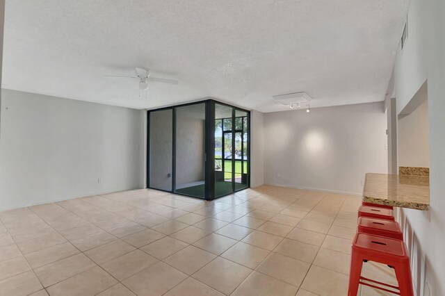unfurnished room with visible vents, a wall of windows, ceiling fan, a textured ceiling, and light tile patterned floors