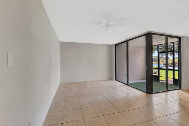 empty room with light tile patterned flooring, ceiling fan, and a wall of windows