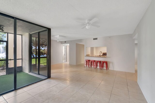 unfurnished room featuring visible vents, a wall of windows, ceiling fan, a sink, and light tile patterned floors