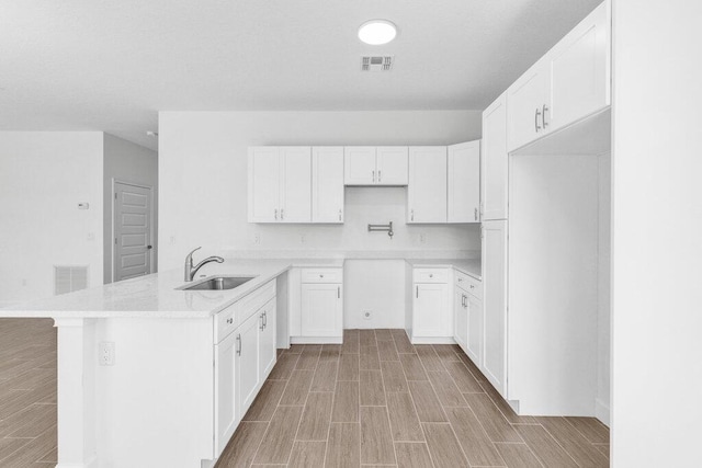 kitchen with a peninsula, wood finish floors, visible vents, and a sink