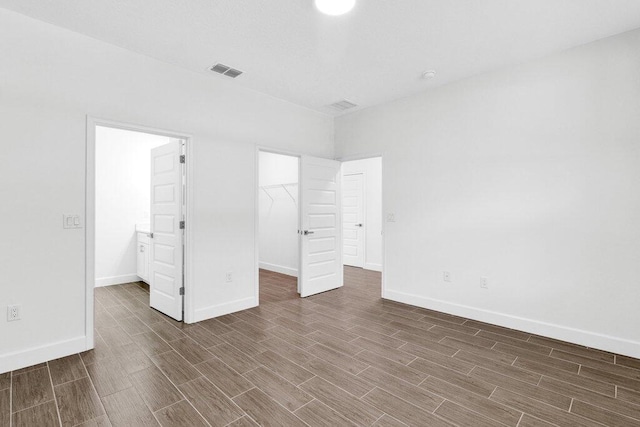 unfurnished bedroom featuring visible vents, baseboards, a walk in closet, and wood finished floors