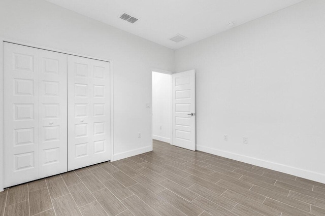 unfurnished bedroom with baseboards, visible vents, wood finished floors, and a closet