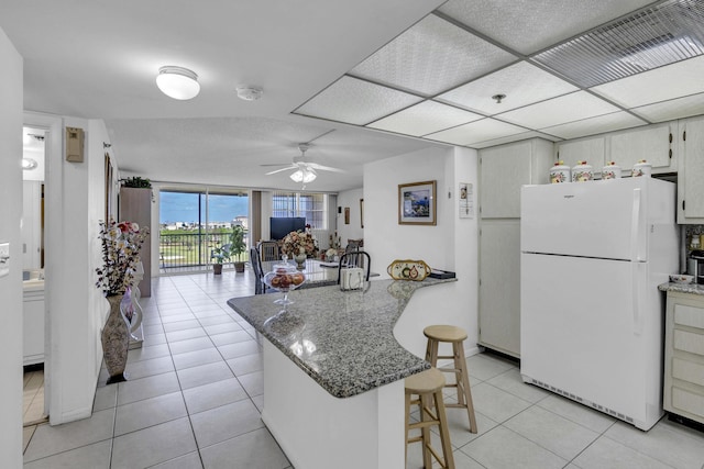 kitchen featuring freestanding refrigerator, a peninsula, a kitchen breakfast bar, ceiling fan, and light tile patterned floors