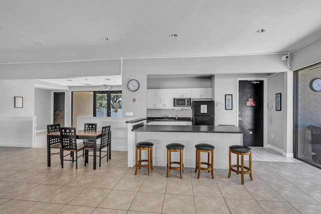 kitchen with dark countertops, stainless steel microwave, freestanding refrigerator, a peninsula, and white cabinetry