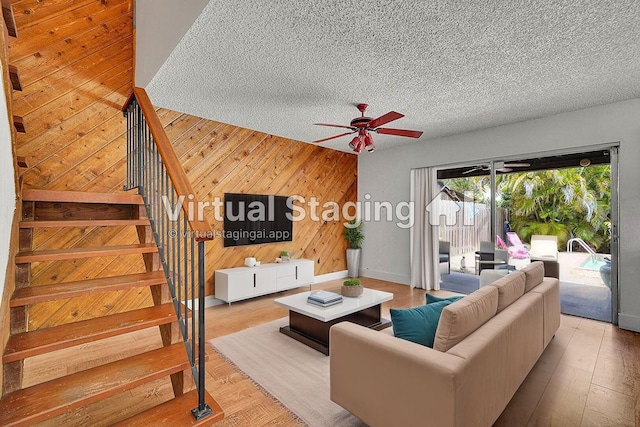 living room with wood walls, wood finished floors, ceiling fan, stairway, and a textured ceiling
