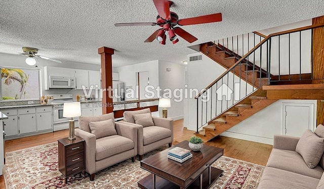 living area with visible vents, stairway, a textured ceiling, a ceiling fan, and light wood-style flooring