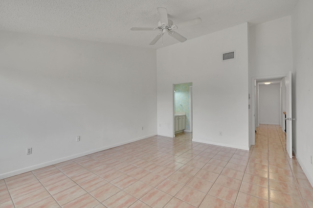 empty room with a textured ceiling, a high ceiling, visible vents, and ceiling fan