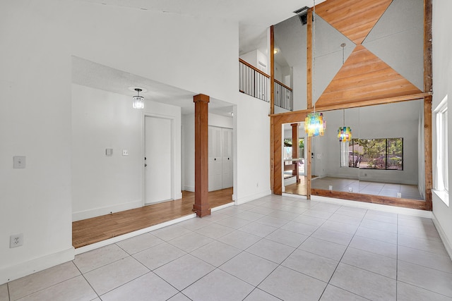 unfurnished living room with tile patterned floors, baseboards, ornate columns, and a high ceiling