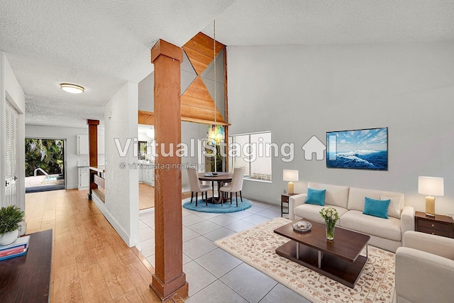 living room with a textured ceiling, decorative columns, baseboards, and a towering ceiling