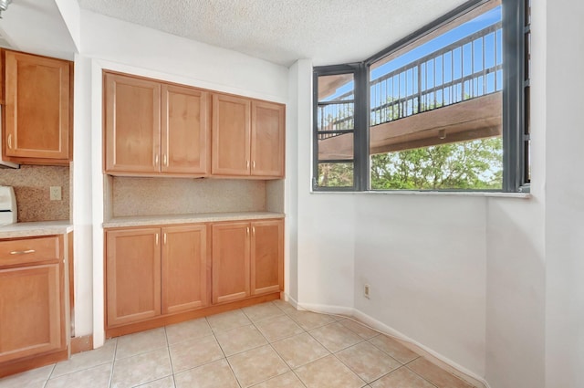 interior space featuring decorative backsplash, a textured ceiling, light countertops, light tile patterned floors, and baseboards