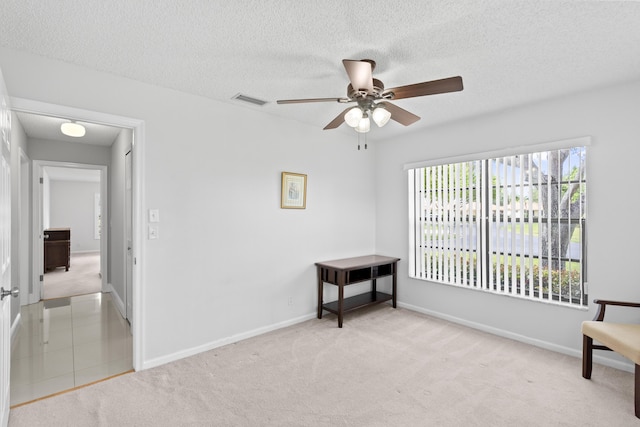 living area featuring carpet floors, a textured ceiling, a ceiling fan, baseboards, and visible vents