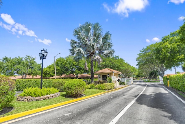 view of street featuring a gated entry, a gate, street lights, and curbs