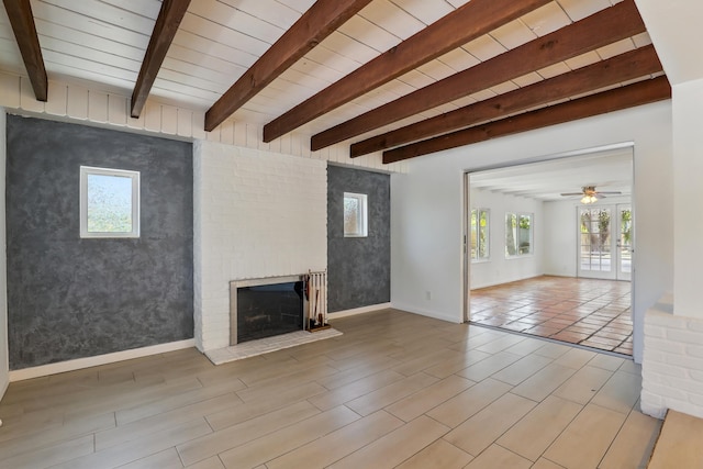 unfurnished living room with ceiling fan, a brick fireplace, beam ceiling, wood finished floors, and baseboards