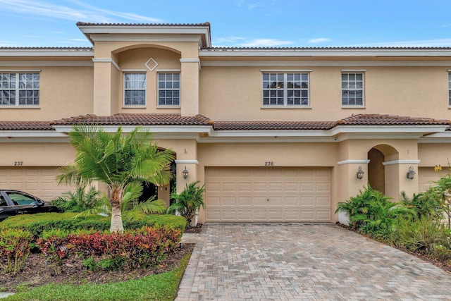view of front facade featuring an attached garage, stucco siding, decorative driveway, and a tiled roof