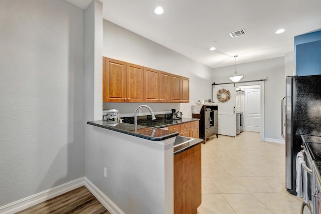 kitchen with brown cabinets, a peninsula, washer / dryer, electric stove, and baseboards