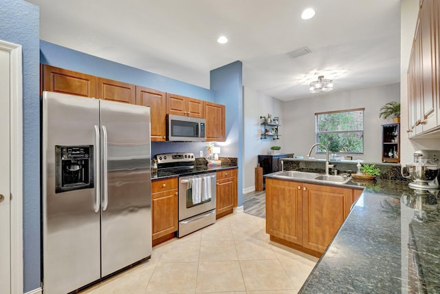 kitchen featuring appliances with stainless steel finishes, a sink, a peninsula, light tile patterned floors, and brown cabinetry