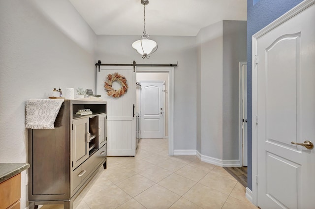 hall featuring a barn door, light tile patterned floors, and baseboards
