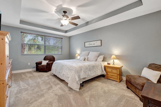bedroom with a tray ceiling, light colored carpet, baseboards, and a ceiling fan
