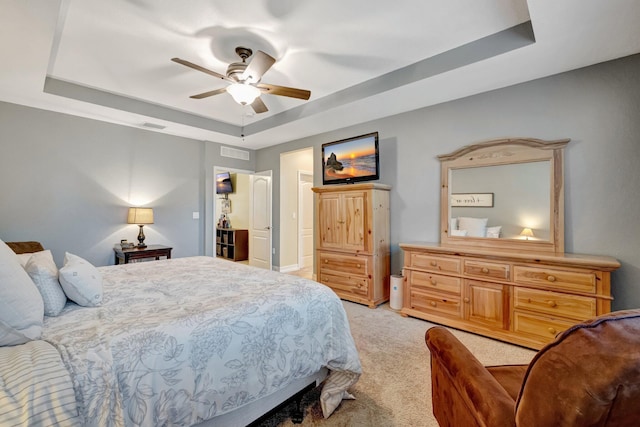 bedroom featuring a raised ceiling, light colored carpet, and ceiling fan