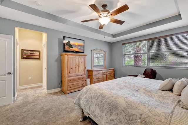 bedroom with light carpet, a raised ceiling, baseboards, and ceiling fan