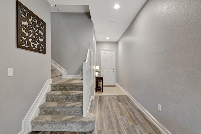 stairway with wood finished floors, baseboards, and recessed lighting