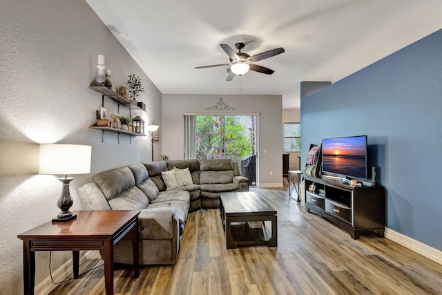 living area featuring ceiling fan, wood finished floors, baseboards, and a textured wall